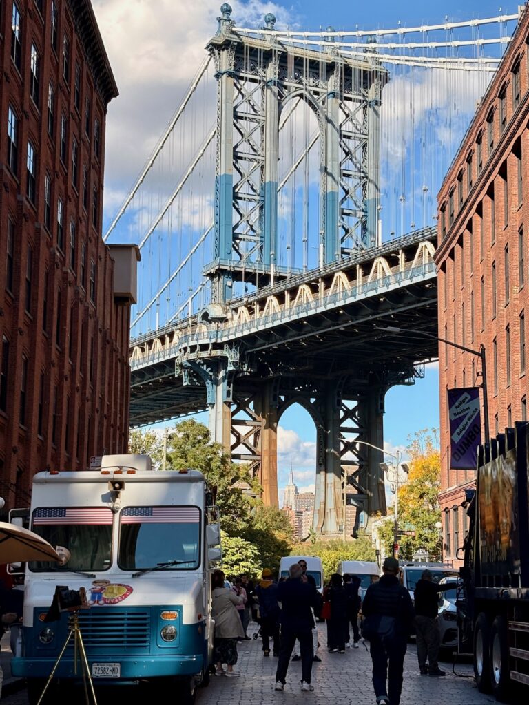 Brooklyn Bridge i baggrunden mellem bygninger og en foodtruck i forgrunden med mennesker omkring, New York City, USA