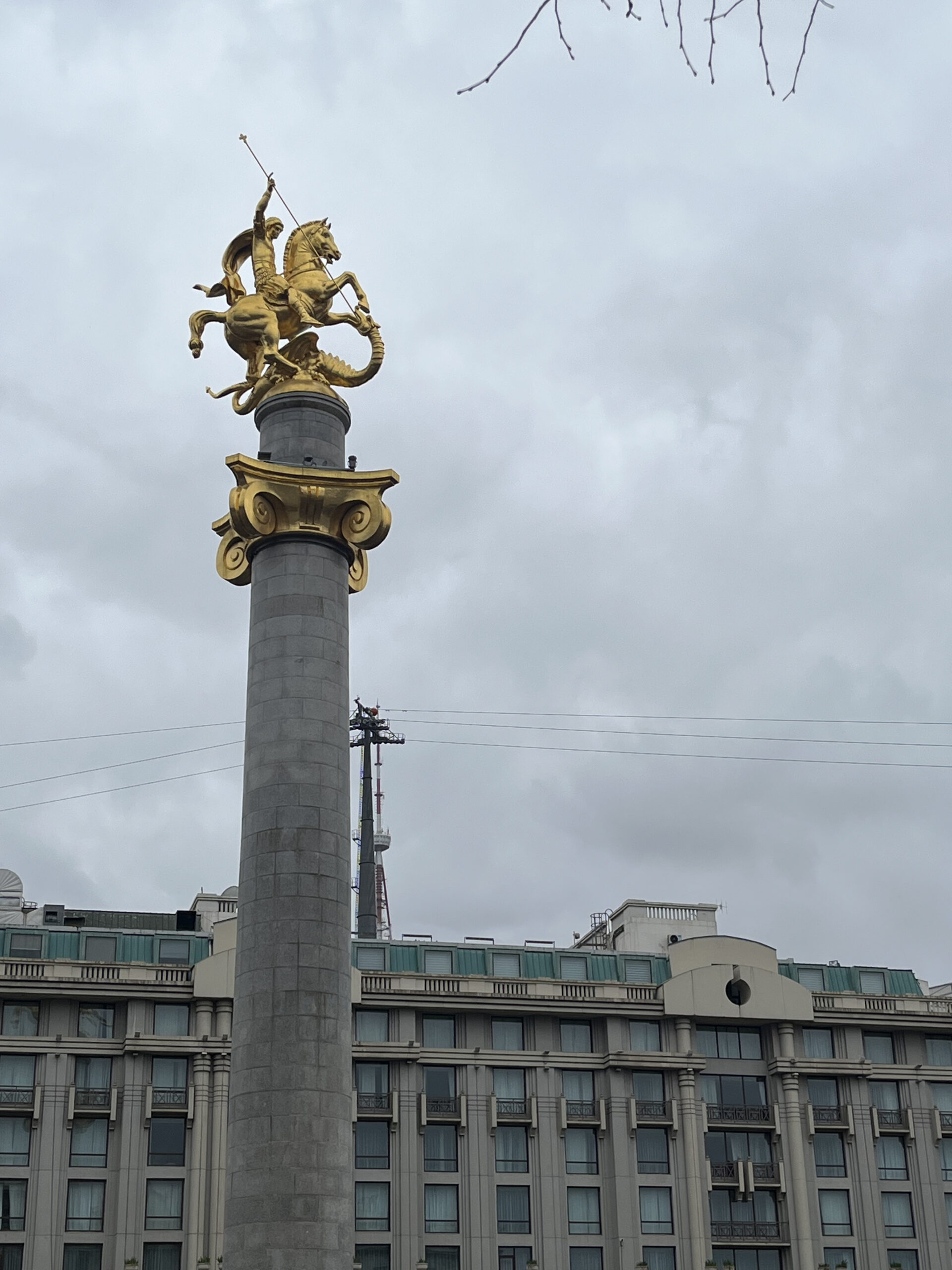 Den gyldne statue af Sankt Georg på en høj søjle mod en grå skyet sky på Frihedspladsen i Tbilisi, Georgien.