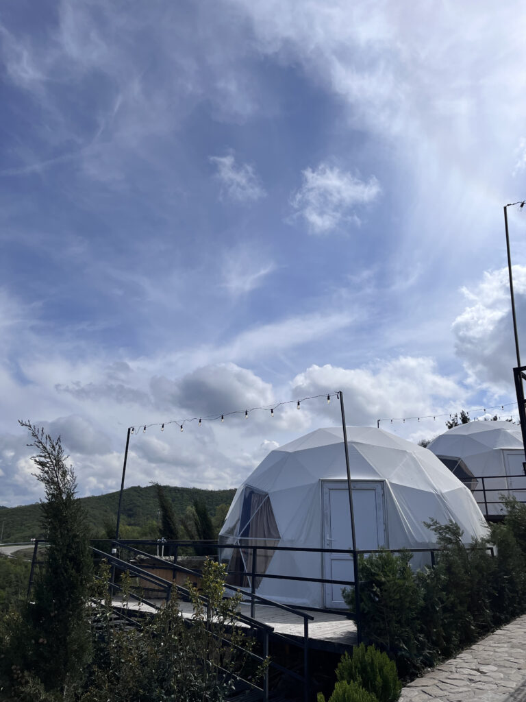 Hvide geodætiske glamping-kugler placeret i grønne bakker under en klar og solrig sky