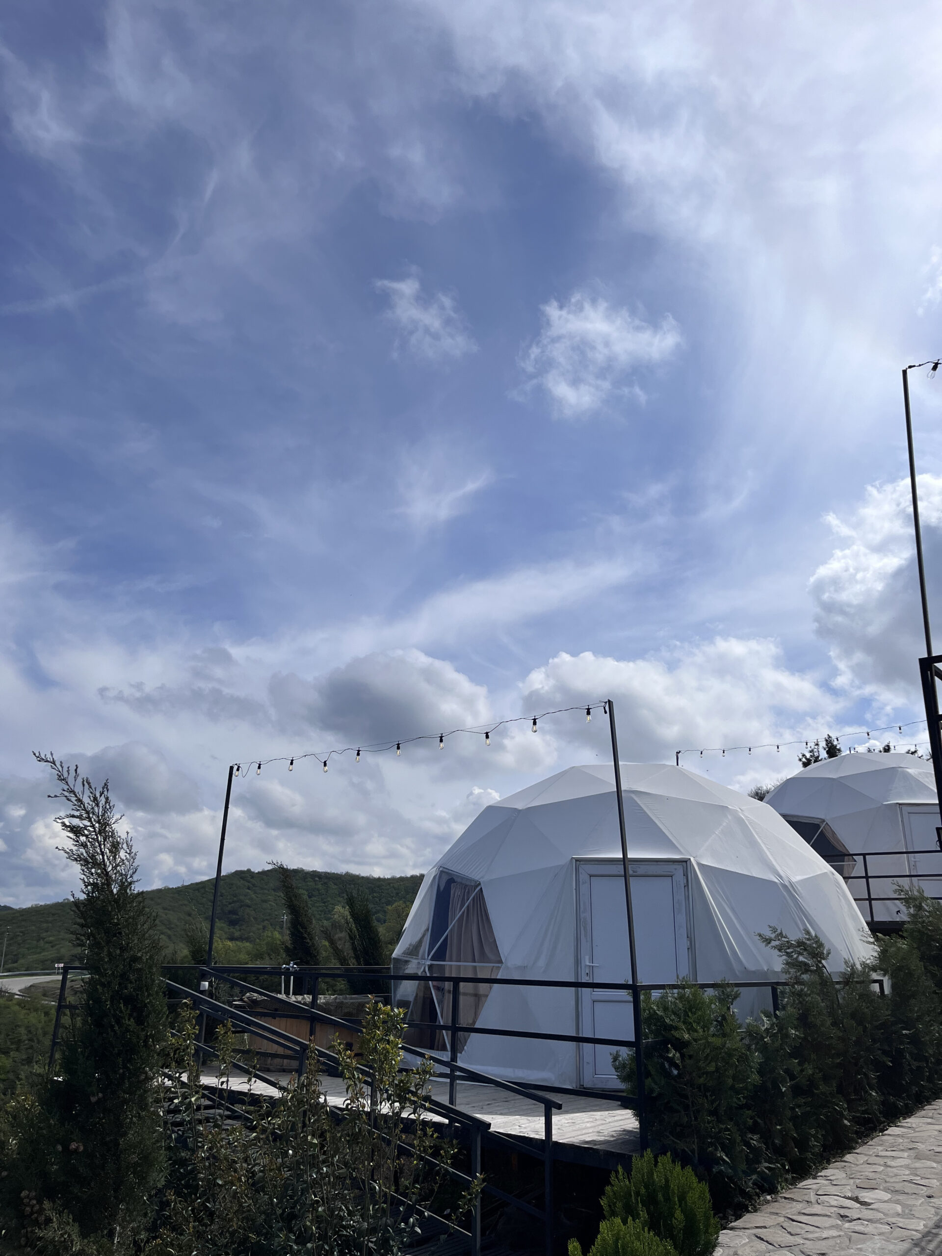 Hvide geodætiske glamping-kugler placeret i grønne bakker under en klar og solrig sky