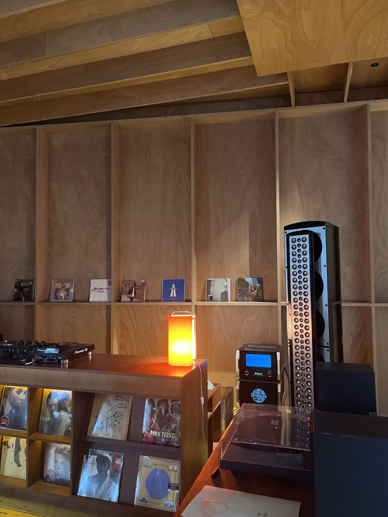 Interiør fra en stilfuld, moderne vinylbar med store højttalere, pladespiller og LP-plader udstillet på lyse træhylder